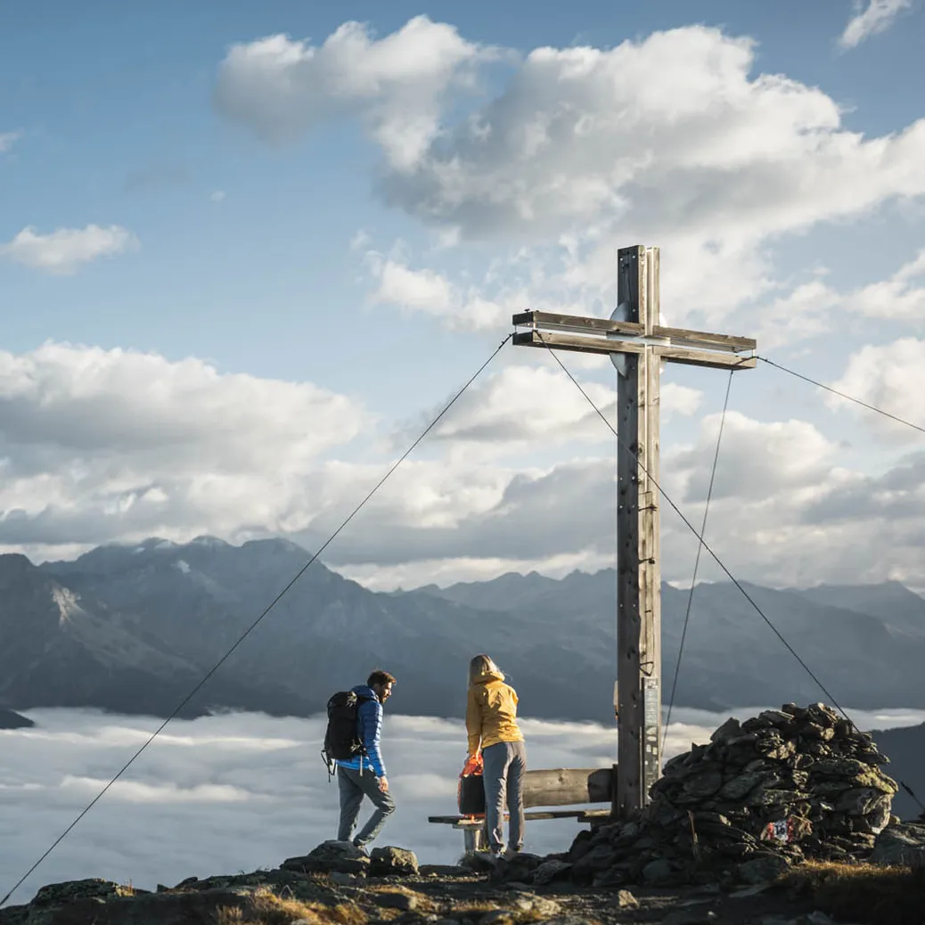 Wanderpaar am Gipfelkreuz über dem Wolkenmeer mit Panoramablick auf die Südtiroler Alpen im Ahrntal