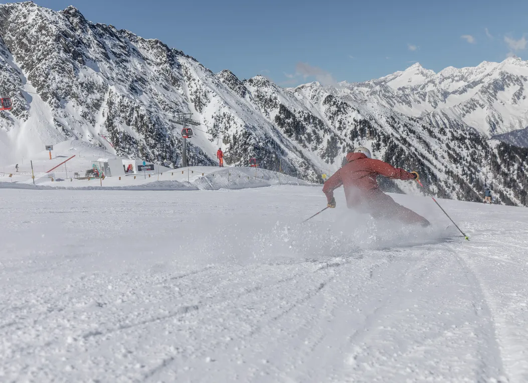 Sciatore in abiti rossi esegue carving su pista battuta al Klausberg con il panorama montano della Val Aurina