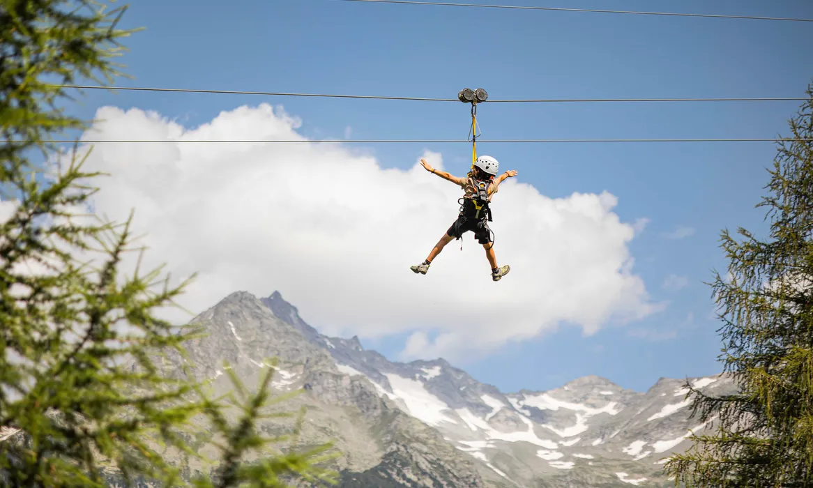 Zipline-Fahrer mit Helm von hinten am Speikboden, Hochgebirgskulisse mit Schneefeldern