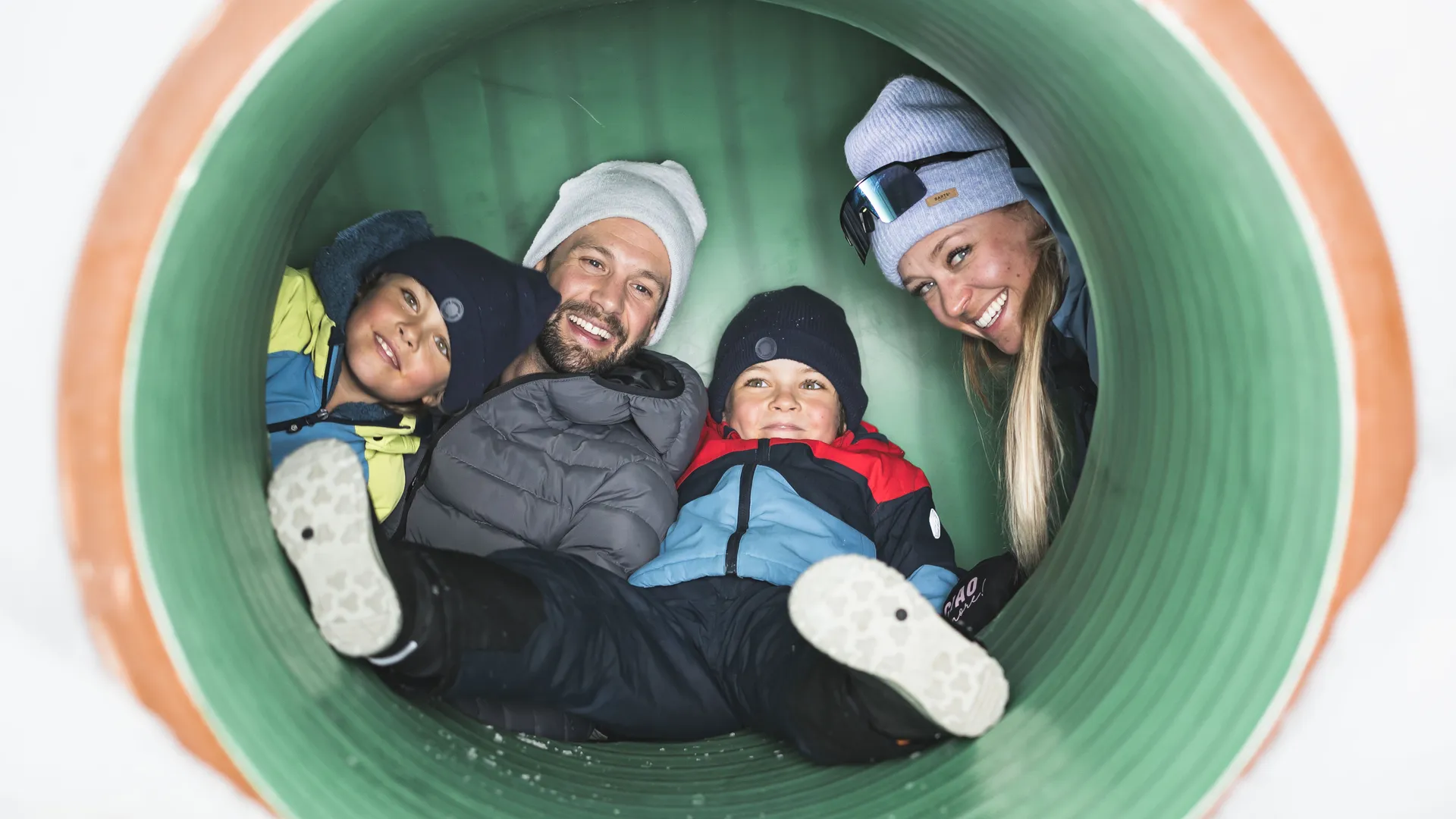 Family laughing from a play tunnel in the children's area of Skiworld Ahrntal in the snow