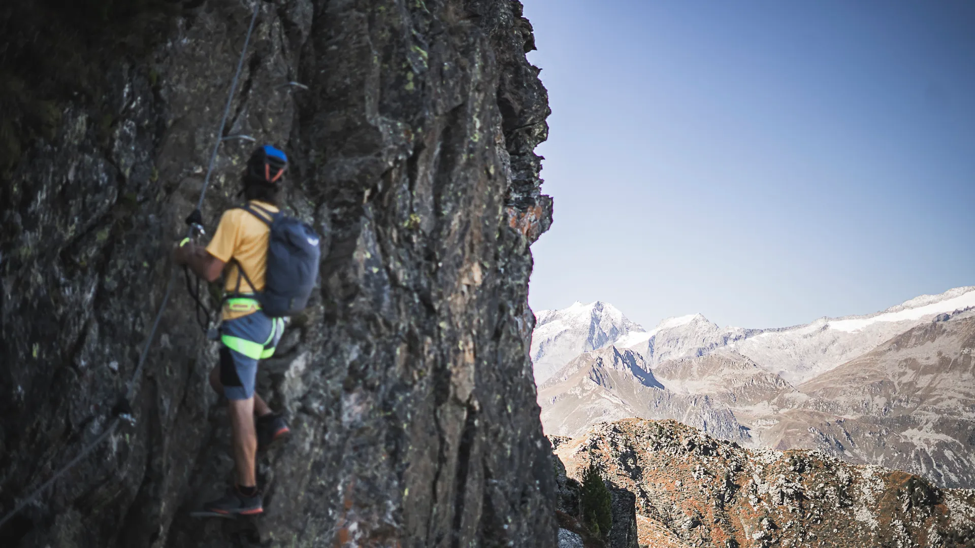 Klettersteiggeher mit Helm an steiler Felswand, schneebedeckte Zillertaler Alpen im Hintergrund