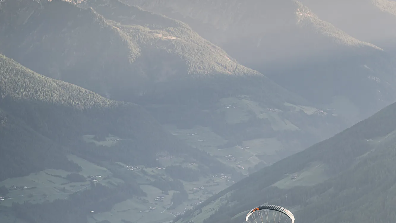 Zwei Paragleiter mit bunten Schirmen in der Abendsonne über dem grünen Ahrntal, Südtirol