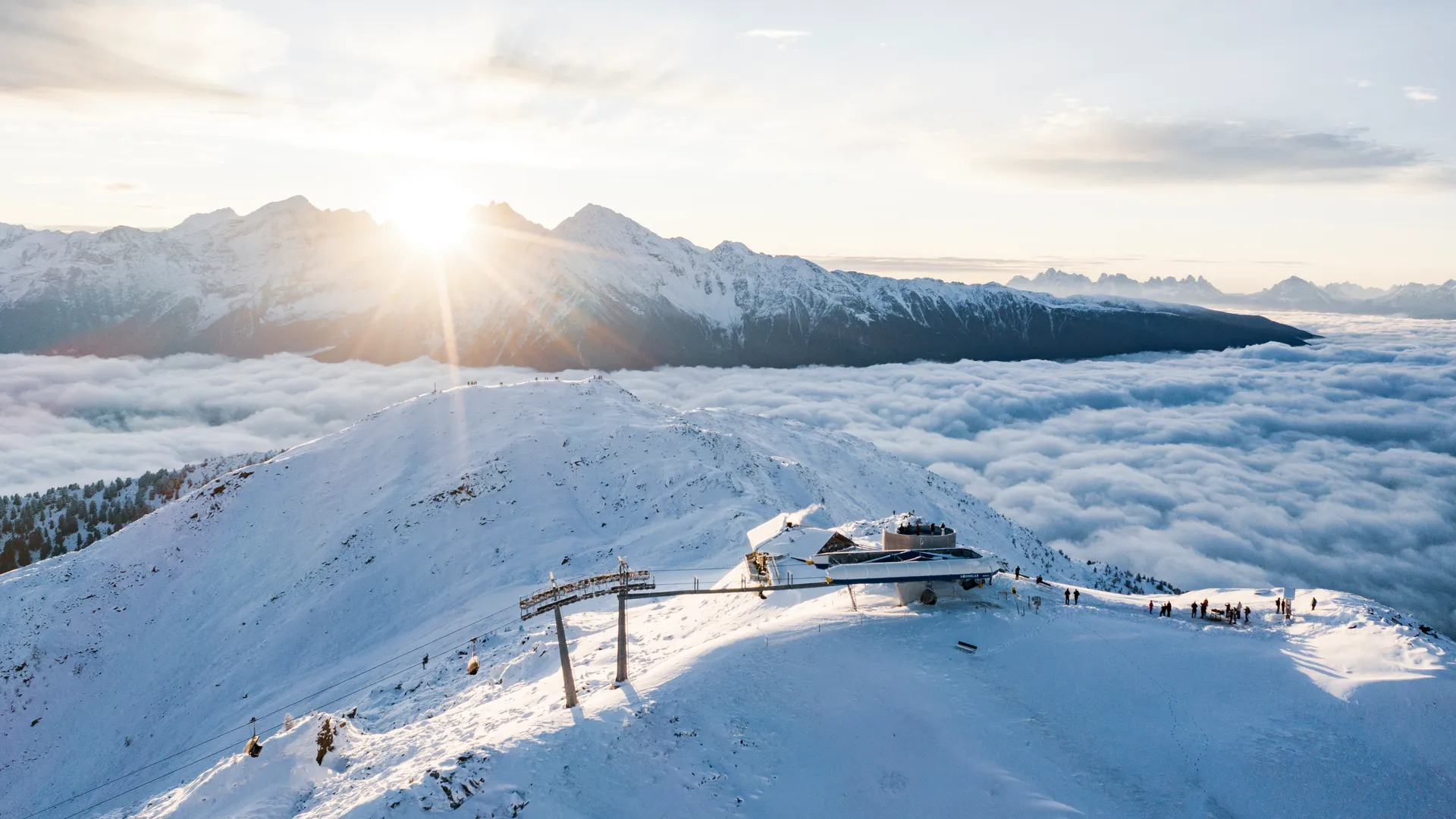 Luftaufnahme der Bergstation Sonnklar bei goldenem Sonnenaufgang über dem Wolkenmeer