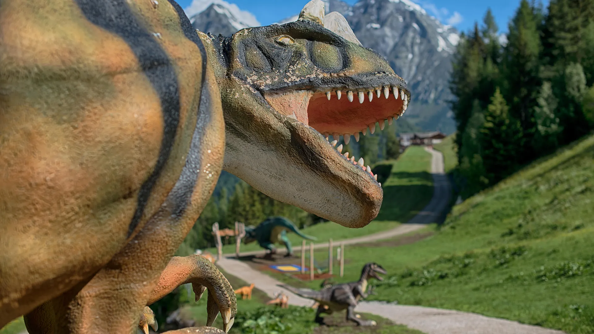 Life-size Allosaurus figure with snow-capped Zillertal Alps peaks in the background at Klausberg