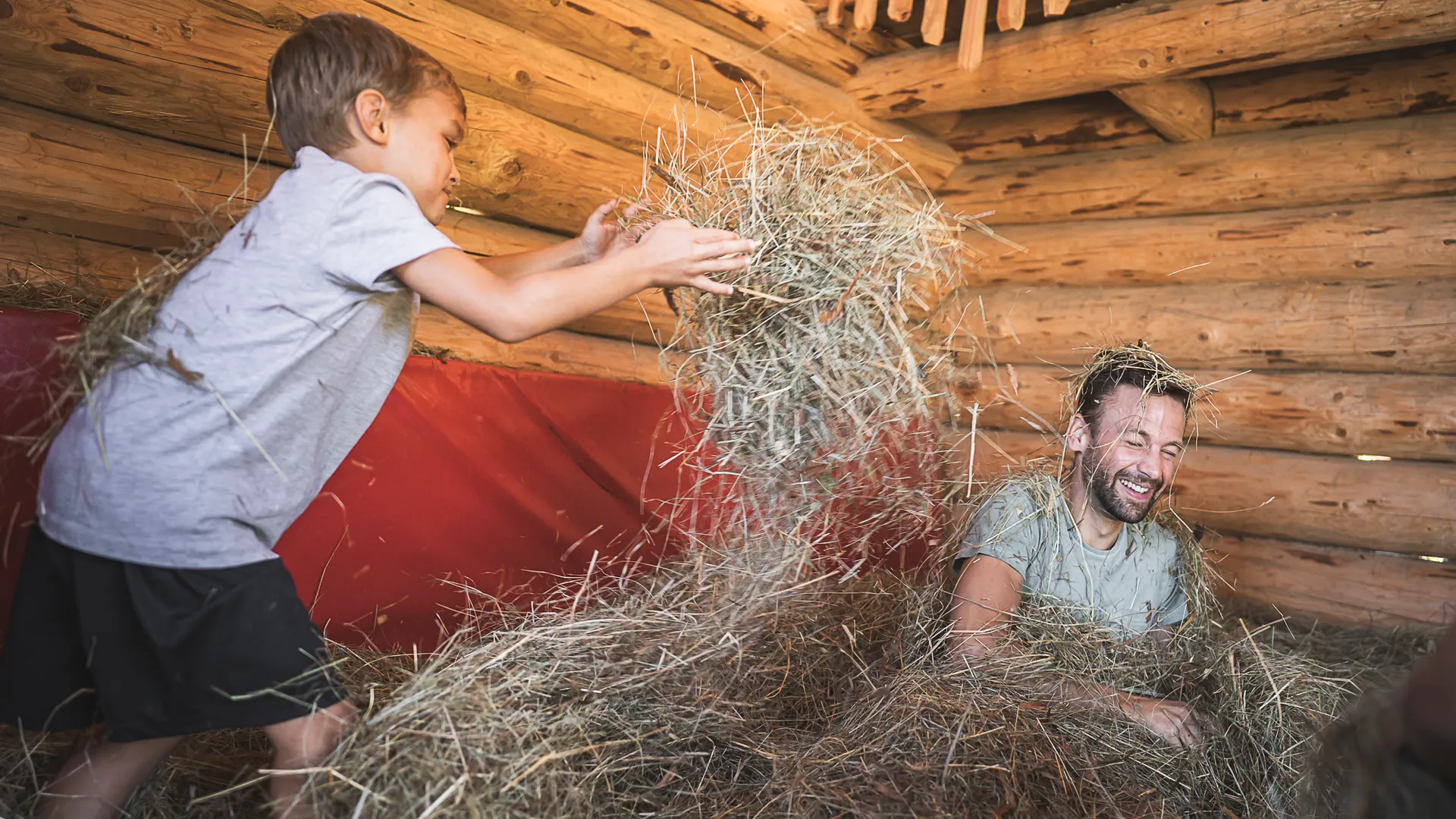 Vater und Sohn haben Spaß beim Spielen im Heu in einer Almhütte