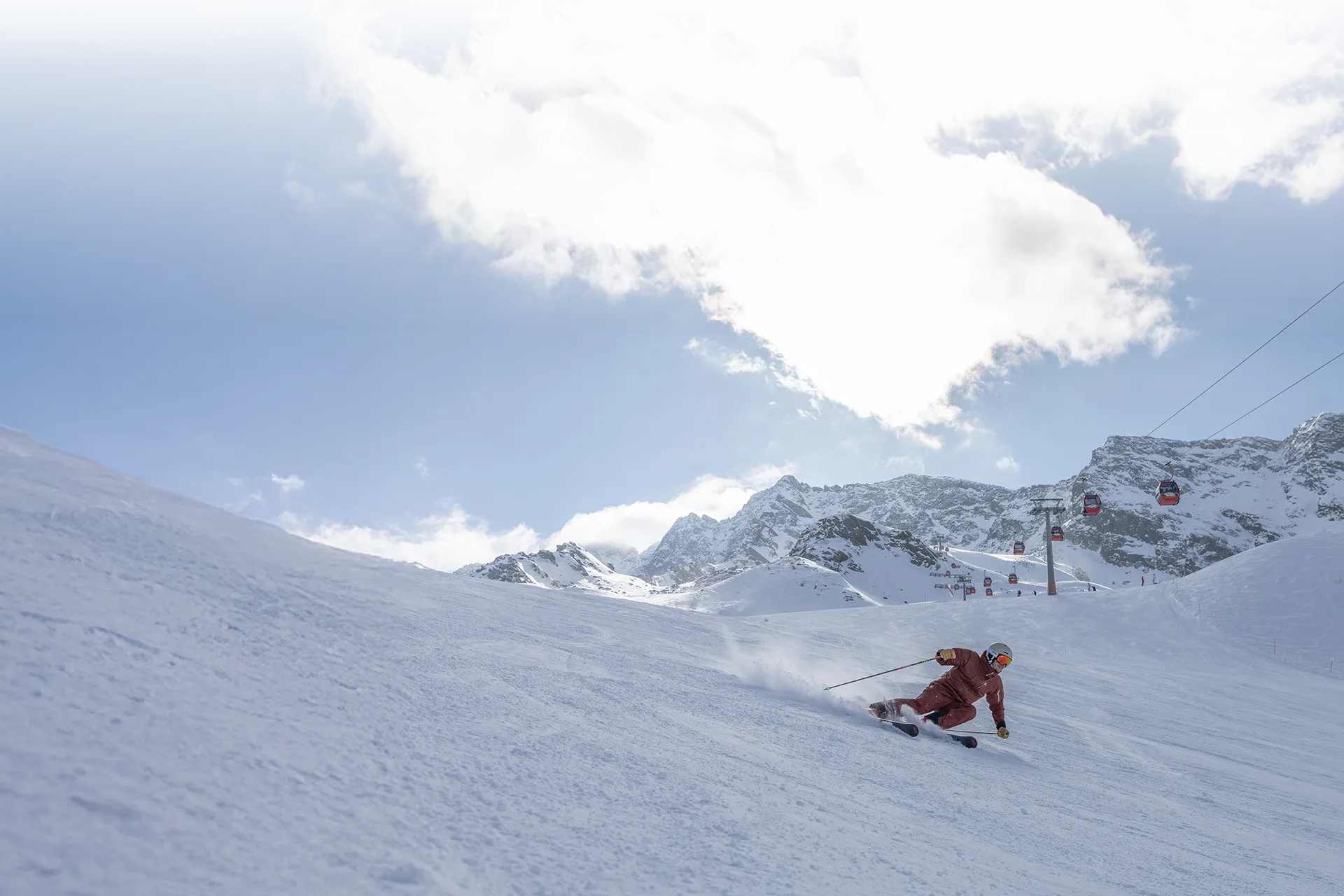 Skier in red ski outfit carving a groomed slope on Klausberg beneath the gondolas