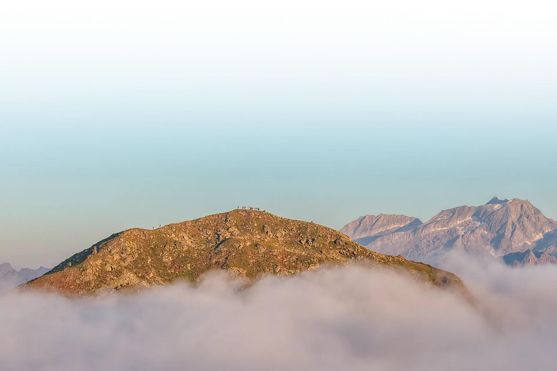 Hiker on a summit above the sea of fog with Zillertal Alps in the morning light