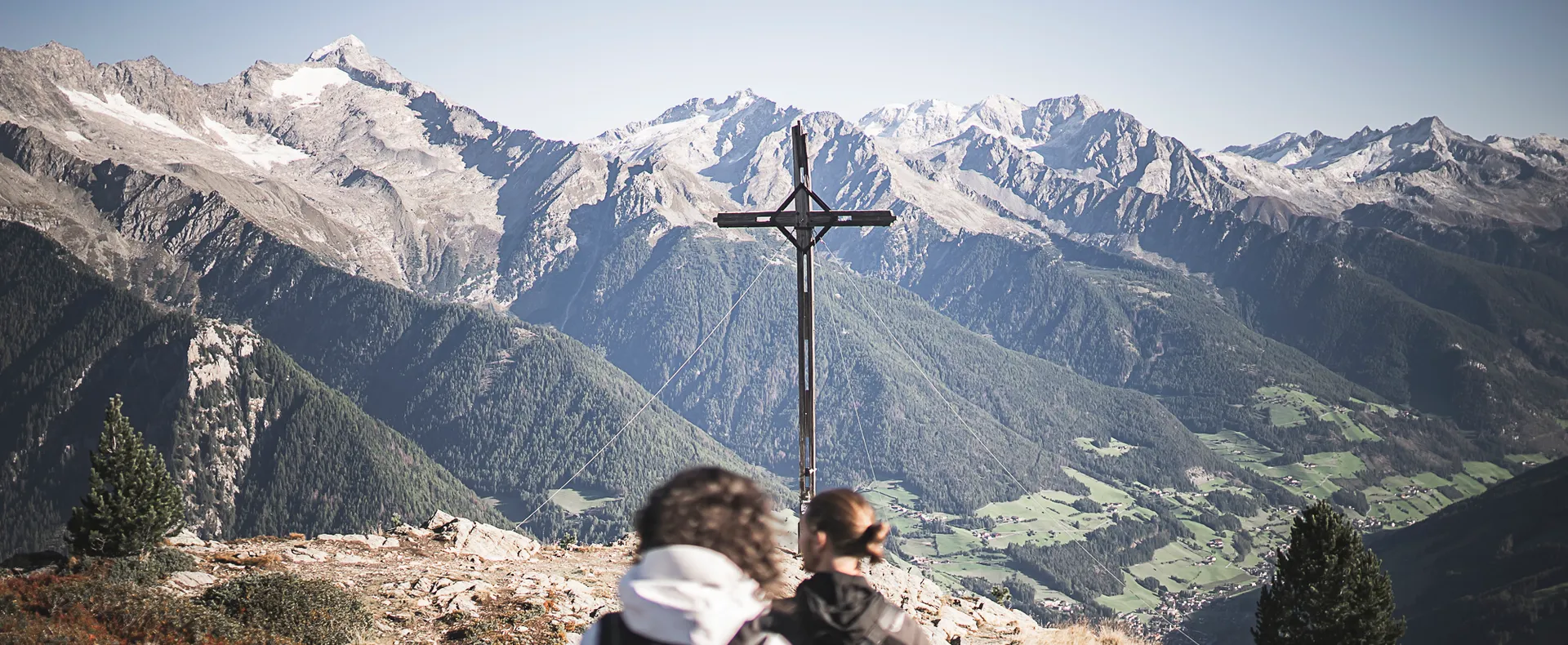 Zwei Wanderer am Gipfelkreuz des Speikbodens mit Blick auf Zillertaler Alpen im Sommer