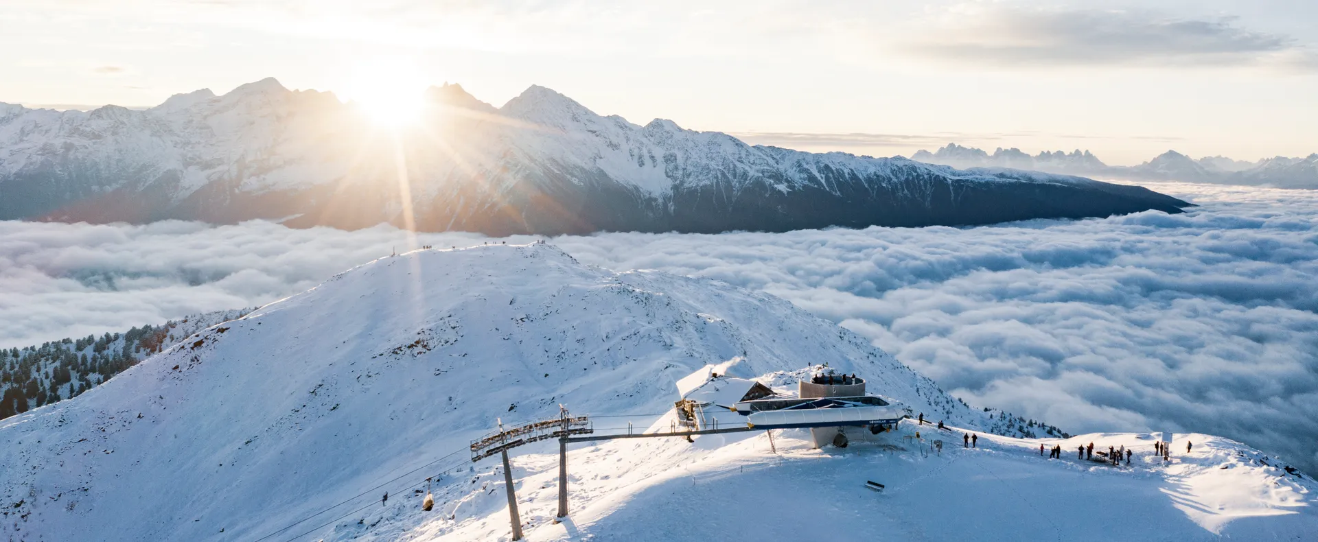 Luftaufnahme der Bergstation Sonnklar bei goldenem Sonnenaufgang über dem Wolkenmeer