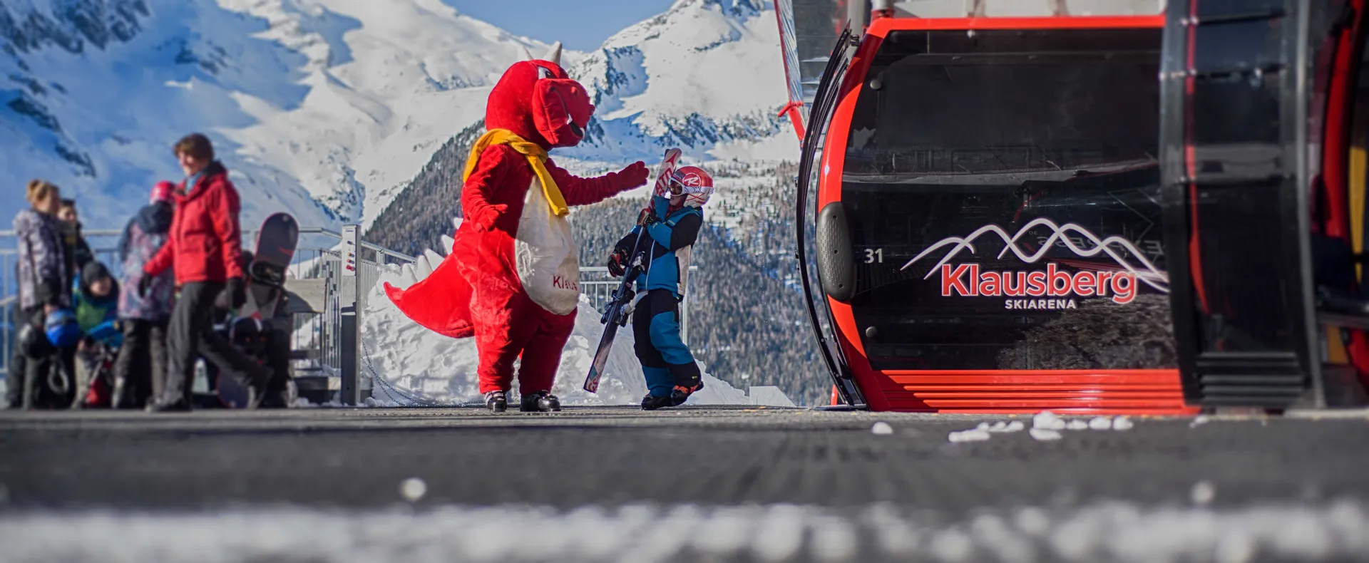 Maskottchen Drache begrüßt Kind an der Klausberg-Bergstation mit Bergpanorama