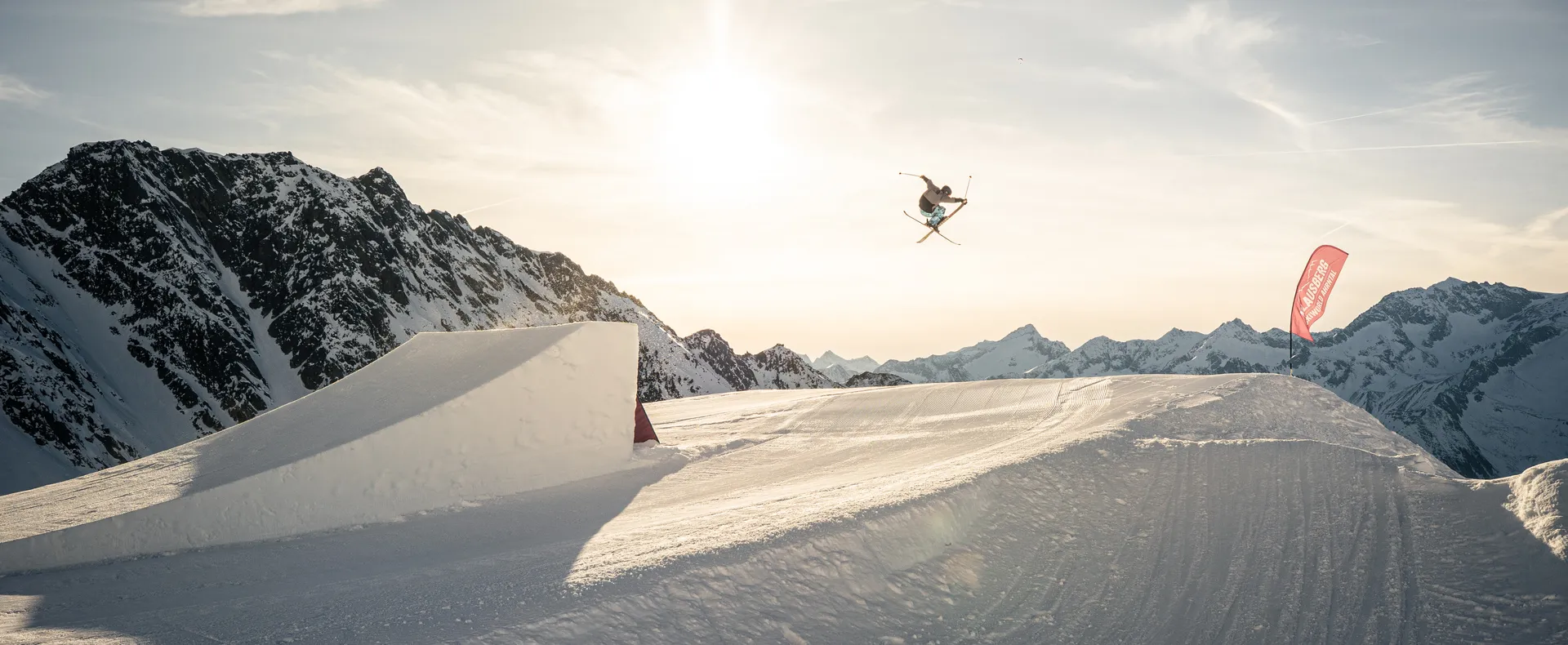 Freestyle-Skifahrer beim Abendsprung am Snowpark Klausberg mit Klausberg-Ahrntal-Beachflag