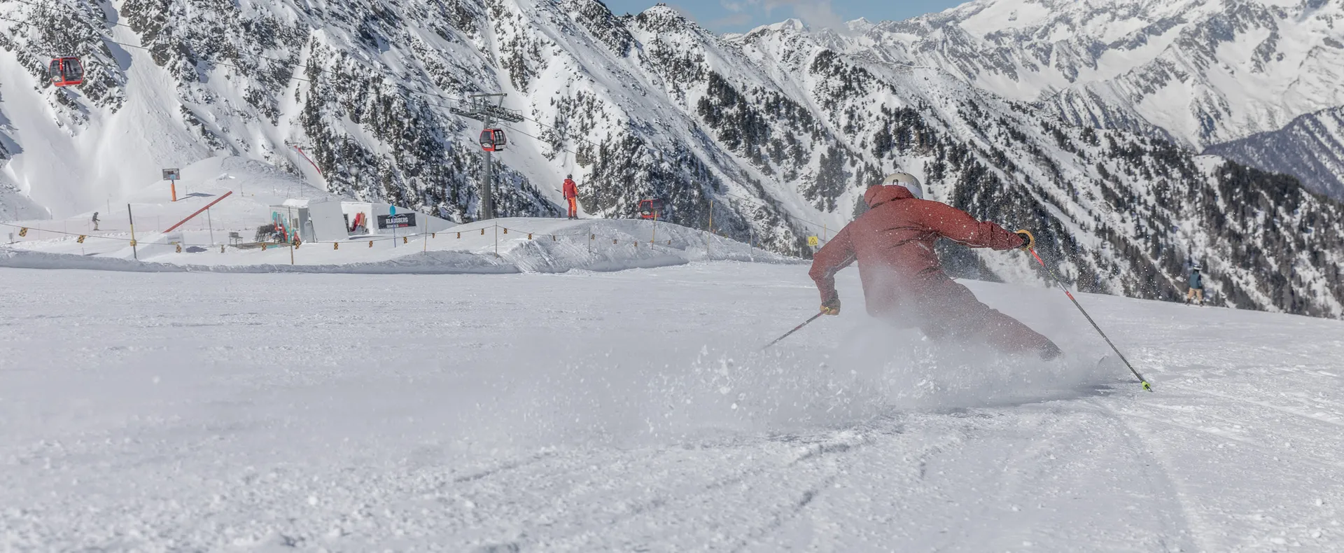 Skifahrer in roter Kleidung carvt auf präparierter Piste am Klausberg mit Ahrntaler Bergpanorama