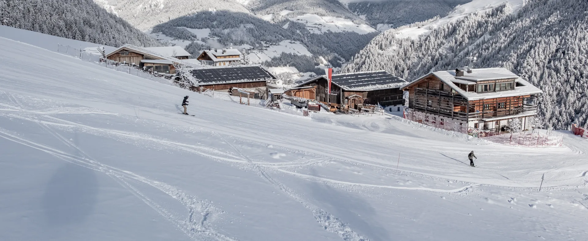 Snowboarder und Skifahrer auf Klausberg-Piste mit Almhütten und verschneitem Ahrntal Panorama