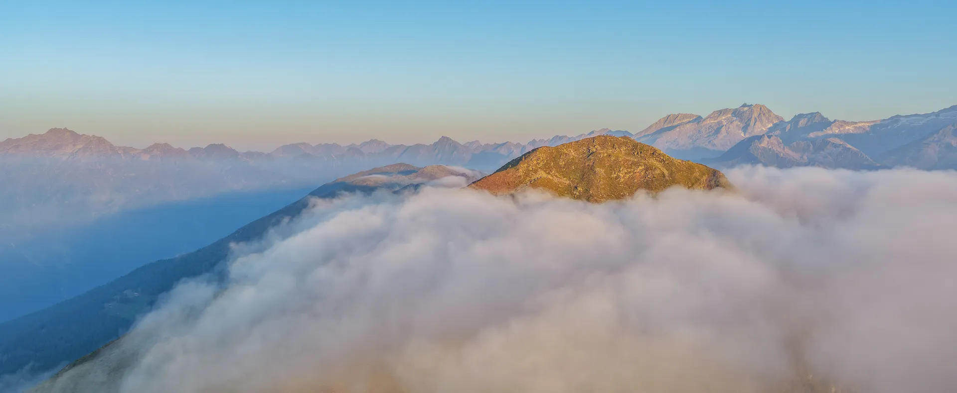 Mountain summit in Ahrntal above the sea of clouds with views of the Zillertal Alps at sunrise