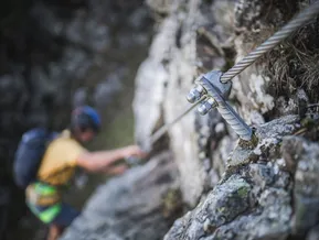 Kletterer greift Felsbolzen am Klettersteig Speikboden — Sicherungsdetail