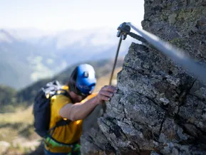 Kletterer am Fels des Klettersteigs Speikboden mit Blick ins Ahrntal