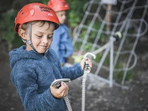 Kind am Klettersteig Speikboden befestigt Karabiner an Stahlseil