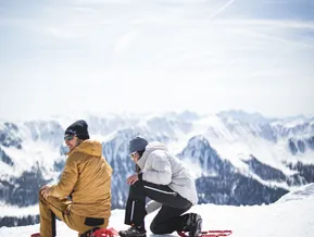 Paar legt rote Schneeschuhe auf Gipfelplateau an, Blick auf die Zillertaler Alpen rund um Klausberg und Speikboden