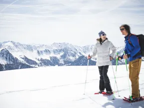 Paar beim Schneeschuhwandern auf sonniger Hochebene im Ahrntal mit Bergpanorama Südtirols