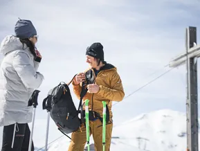 Bergführer erklärt Schneeschuh-Ausrüstung am Gipfelkreuz des Speikboden an einem sonnigen Wintertag