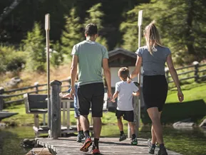Family walks along a wooden boardwalk at the mountain lake in Ahrntal
