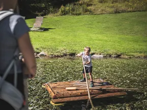 Boy punts a wooden raft across the mountain lake at Klausberg family park