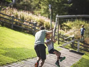 Child on zip line at Klausberg mountain playground, father helps push
