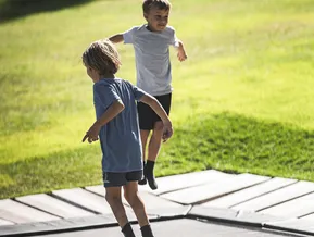 Two children jumping happily on ground trampoline on green meadow at family park in Ahrntal
