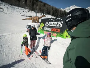 Familie vor dem Dino-Sun-Line-Banner am Klausberg – Skiworld Ahrntal mit Dinosaurier-Themenbereich