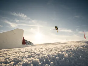 Freestyle-Skifahrer beim Cross-Trick über den Snowpark-Kicker am Klausberg bei Sonnenuntergang