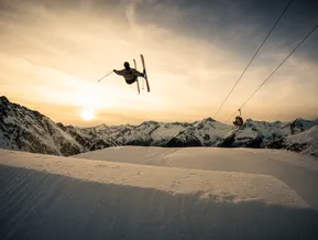 Freestyle-Skifahrer im Cross-Trick mit Gondeln der Klausberg-Seilbahn im Abendpanorama