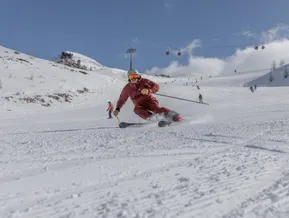Skifahrer in rotem Anzug carvt auf präparierter Piste mit Gondelbahn im Hintergrund