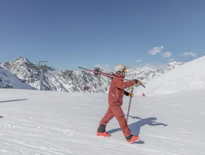 Skifahrer mit Ski über der Schulter auf sonniger Piste am Speikboden mit Blick auf Zillertaler Alpen