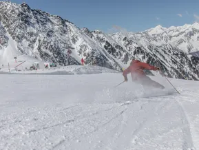 Skifahrer in roter Kleidung carvt auf präparierter Piste am Klausberg mit Ahrntaler Bergpanorama