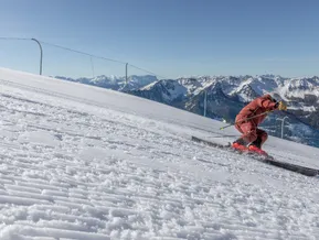 Skifahrer im roten Anzug beim Carving auf perfekt präparierter Piste am Klausberg