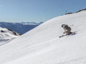 Skifahrer in dynamischer Carving-Haltung auf breiter Piste mit Dolomiten-Panorama