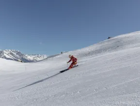 Skifahrerin in roter Kleidung auf frisch präparierter Piste am Klausberg mit Bergpanorama