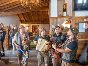 Südtiroler Volksmusiker in Tracht spielen Akkordeon und Gitarre in urigem Almhütten-Interieur