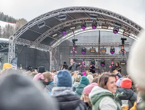 Live-Konzert-Bühne mit Band und pinkfarbenen Scheinwerfern, jubelnde Menge auf der Skipiste