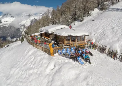 Sonnenterrasse einer Berghütte mit Skiern im Ständer und Alpenpanorama im Hintergrund