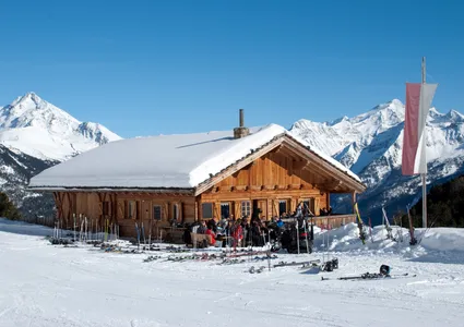 Skihütte mit Terrasse und abgestellten Skiern, südtiroler Fahne, Alpenpanorama