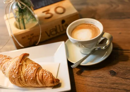 Croissant und Cappuccino auf Holztisch in gemütlicher Almhütten-Atmosphäre