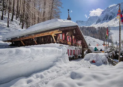 Rustikale Skihütte mit Tirol-Fahne, Holzdekoration und Gästen auf der Terrasse