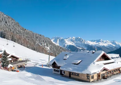 Skigebiet-Panorama mit mehreren Berghütten, Pisten und Sessellift unter strahlend blauem Himmel