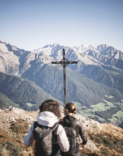 Zwei Wanderer am Gipfelkreuz des Speikbodens mit Blick auf Zillertaler Alpen im Sommer