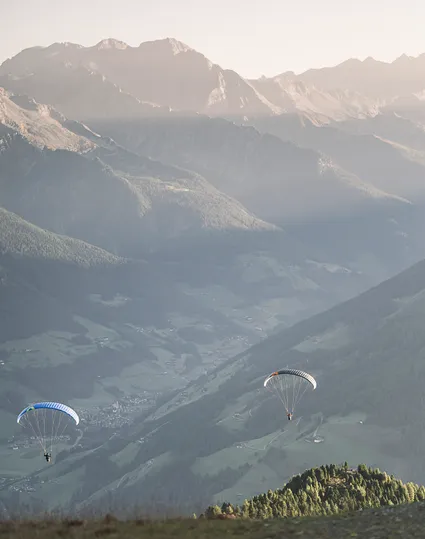 Zwei Paragleiter mit bunten Schirmen in der Abendsonne über dem grünen Ahrntal, Südtirol
