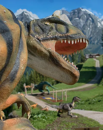 Lebensgroße Allosaurus-Figur mit schneebedeckten Gipfeln der Zillertaler Alpen im Hintergrund am Klausberg