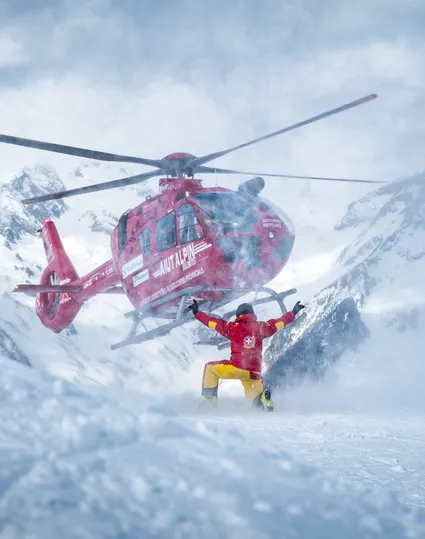 Red rescue helicopter Aiut Alpin Dolomites landing in deep snow during slope rescue operation