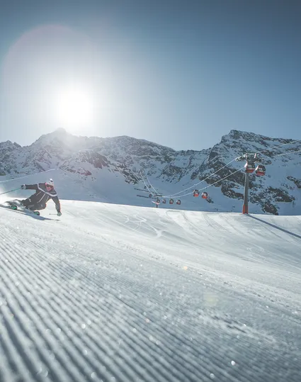 Skifahrer beim Carvingschwung auf der Klausberg-Piste neben der Gondelbahn, sonniger Wintertag