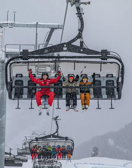 Skifahrer auf Sessellift am Speikboden bei Schneefall mit jubelndem Skilehrer in roter Uniform